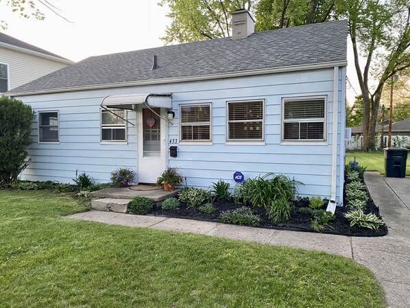 A single-story house with a front porch, a small garden, and a mailbox.