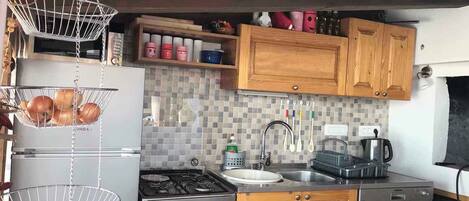 A compact kitchen with wooden cabinets, a gas stove, a sink, and hanging baskets.