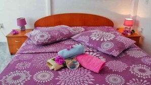 A neatly made bed with a purple floral bedspread and matching pillows, a wooden headboard, and two bedside lamps with pink shades. - Holiday apartment With sea view and terrace (Komarna)
