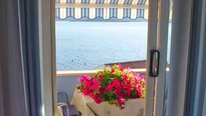 A balcony with a table and chairs, a flower pot with pink flowers, and a view of the sea. - Holiday apartment With sea view and terrace (Komarna)