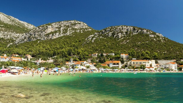 A coastal town with clear turquoise waters, a sandy beach, and buildings with red roofs. - Holiday apartment With sea view and terrace (Komarna)