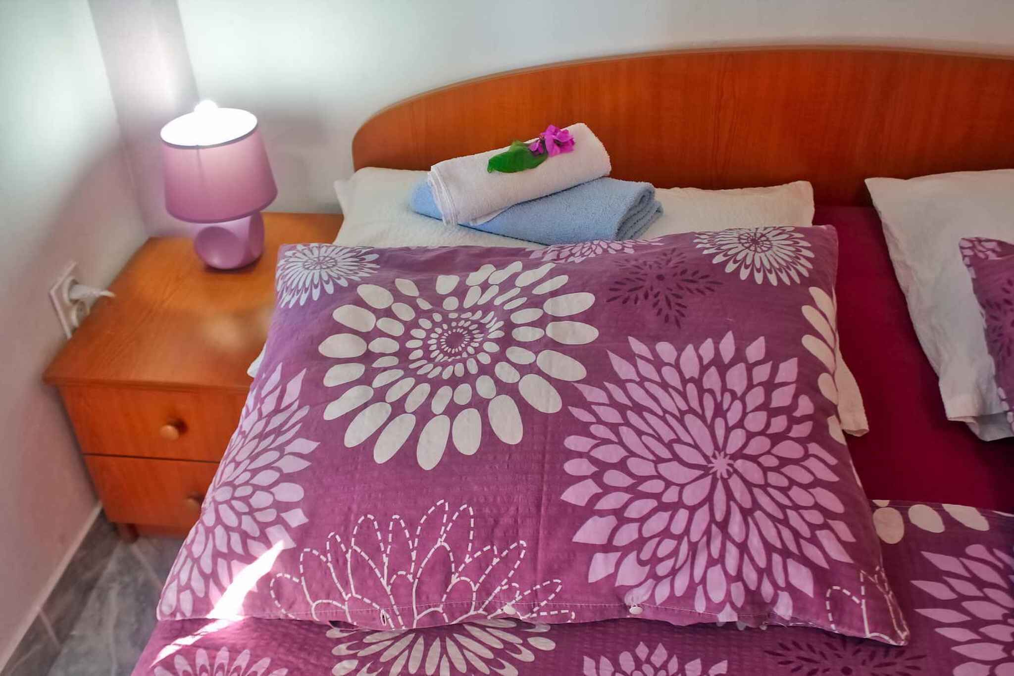 Ein ordentlich bezogenes Bett mit blumigen Kissen und einem auf dem Kopfteil gefalteten Handtuch.