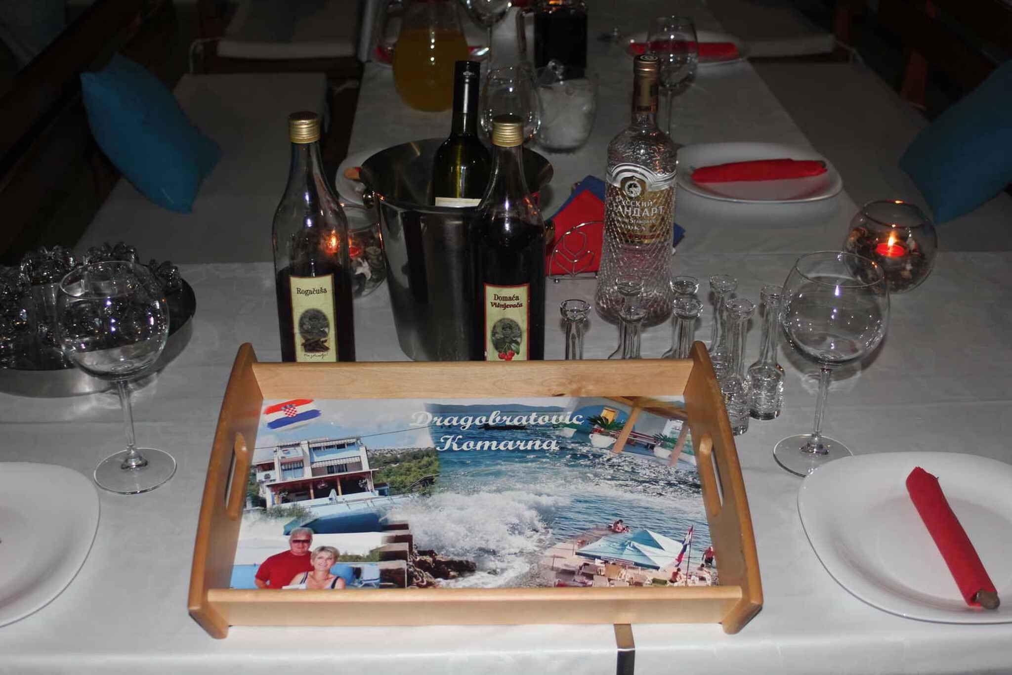 A dining table set with wine bottles, glasses, and a framed picture of a coastal scene.