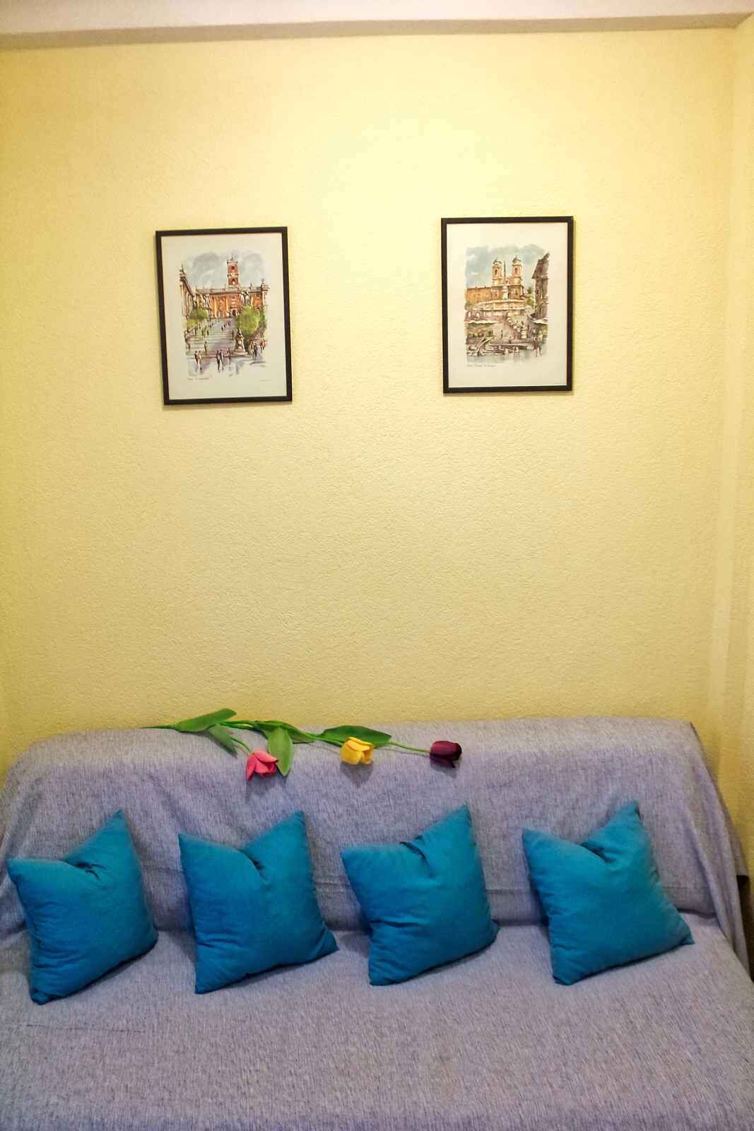Une pièce avec un canapé gris, quatre coussins bleus et deux tableaux encadrés accrochés au mur.