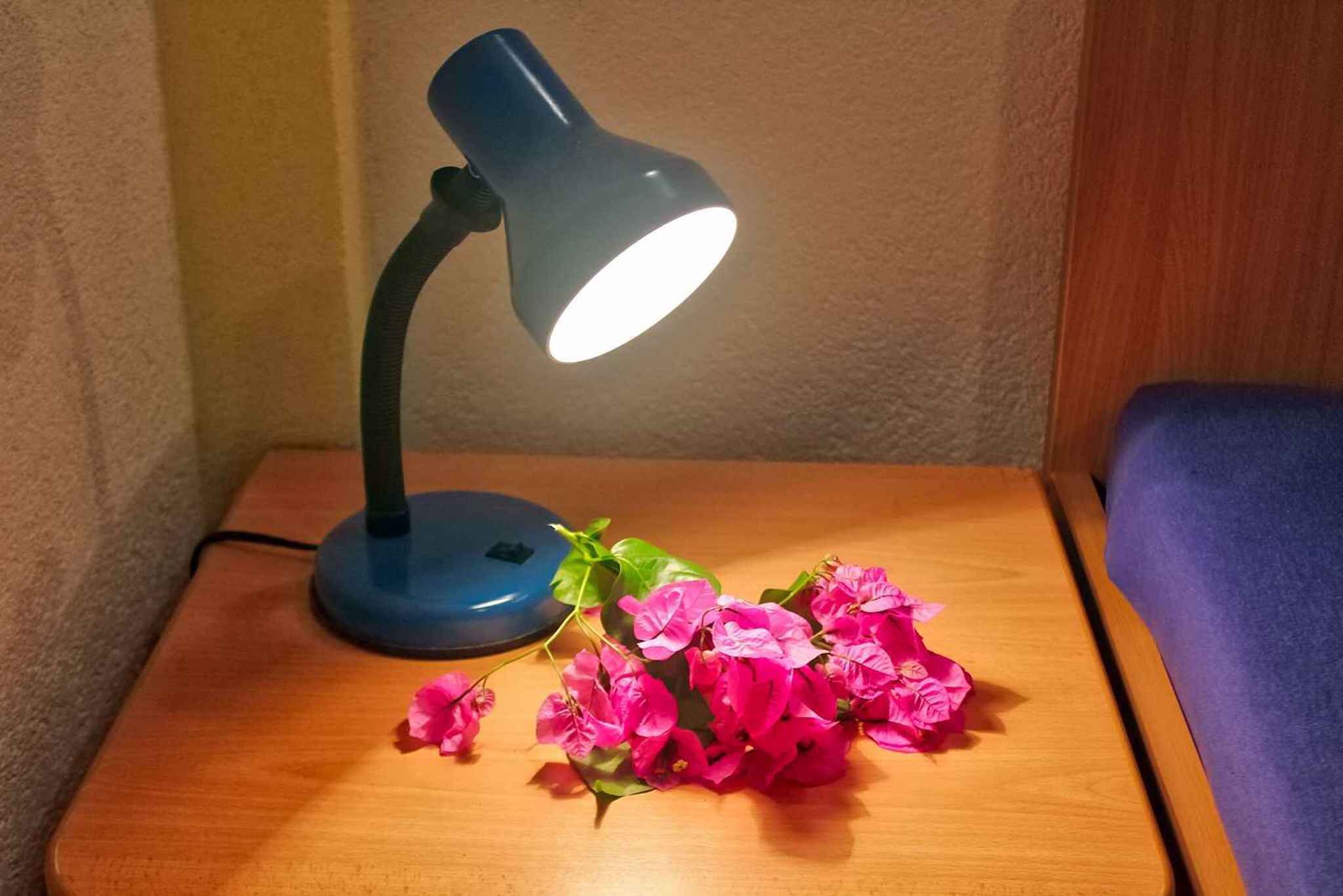 En skrivebordslampe på et natbord med en vase med lyserøde blomster.