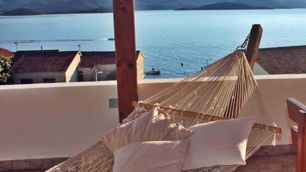 A hammock with pillows on a balcony overlooking a body of water and buildings. - Holiday apartment only 50 m from the sea (Komarna)