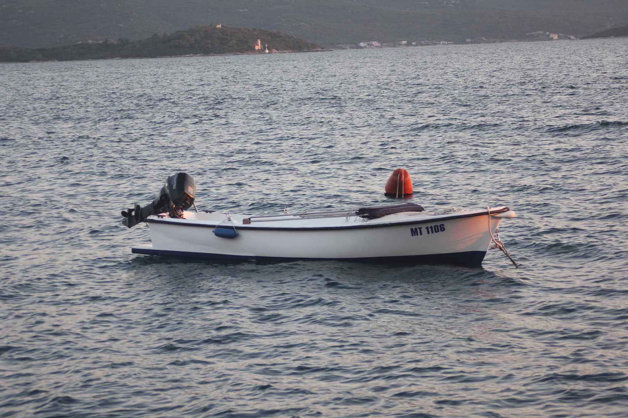 Un petit bateau à moteur avec une personne à bord, flottant sur une eau calme.
