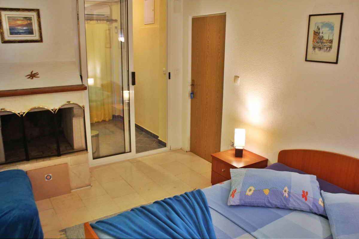 A hotel room with a bed, a small bedside table with a lamp, a sliding glass door leading to a balcony, and a framed picture on the wall.