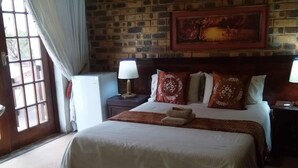 A bedroom with a large bed, a brick wall, a window with curtains, and a painting above the bed.