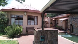 A house with a swimming pool, a patio with a bench, and a covered area.