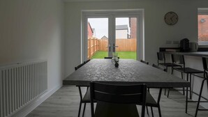 A modern kitchen with a large dining table, black chairs, a clock on the wall, and a view of the backyard. - Beautiful 4-bed House 15 Mins to Cardiff & Newport (Cardiff)