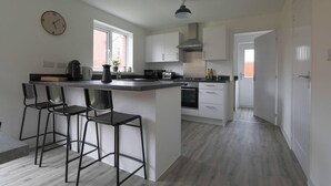 A modern kitchen with a central island, bar stools, a clock, and a view to the outside. - Beautiful 4-bed House 15 Mins to Cardiff & Newport (Cardiff)