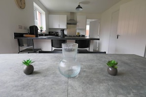 A modern kitchen with white cabinets, a black countertop, and a central island. There are two potted plants on the island. - Beautiful 4-bed House 15 Mins to Cardiff & Newport (Cardiff)