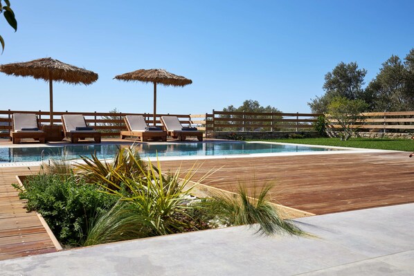 Zona de piscina amb terrassa de fusta, gandules i sobris de palla.