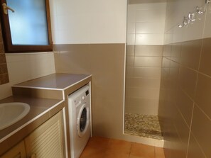 Une petite salle de bain comprenant un lave-linge, un lavabo et un espace douche.
