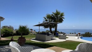 En udendørs terrasse med pool, siddeområde og havudsigt.