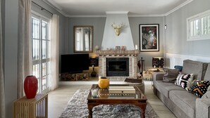 En stue med pejs, sofa, fjernsyn og en rød vase.