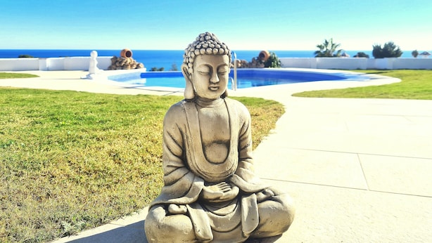 En Buddha-statue i en have med swimmingpool og havudsigt.
