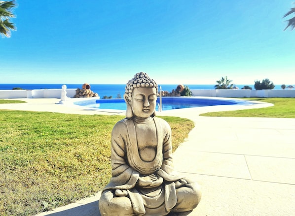 Buddha-patsas puutarhassa, jossa on uima-allas ja näkymä merelle.