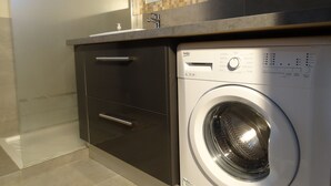 A modern kitchen with a built-in washing machine, a countertop, and a tiled backsplash. - Maison Corse n°4 (Propriano)