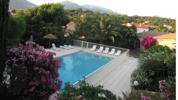 A swimming pool with lounge chairs, surrounded by lush greenery and mountains in the background. - Maison Corse n°4 (Propriano)