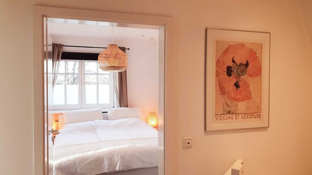 A bedroom with a bed, a hanging light fixture, a window with curtains, and a framed picture on the wall. - Traumhafte Ferienwohnung vor den Toren Lübecks (Wesenberg)