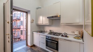 A compact kitchen with white cabinets, a gas stove, an oven, and a small countertop with a kettle and a coffee maker. - Cozy studio in Fondazione Prada district (Milano)