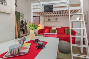 Ein gemütliches Zimmer mit einem Etagenbett, einem Esstisch mit Tassen und Untertassen sowie einem roten Sofa.