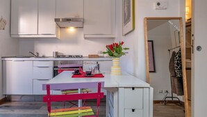 A modern kitchen with white cabinets, a wooden table, and a colorful chair. - Cozy studio in Fondazione Prada district (Milano)