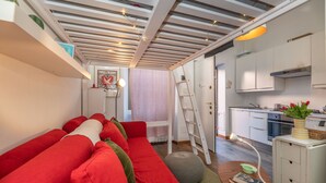 A compact living space with a red sofa, a ladder, a kitchen area, and a skylight. - Cozy studio in Fondazione Prada district (Milano)