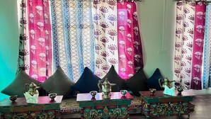 A traditional room with a sofa set, a wooden table with decorative items, and patterned curtains. - Tongspon Camp (Leh)