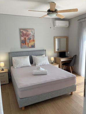 A neatly arranged bedroom with a bed, bedside tables, a desk, a chair, a ceiling fan, and a wall-mounted air conditioner. - ZAX SEA VIEW 4 villa complex, Heated pool and 8 bedrooms (ierapetra)