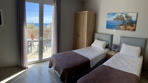 A hotel room with two beds, a wooden wardrobe, a painting of a coastal scene, and a view of the outdoors through a sliding door. - ZAX SEA VIEW 4 villa complex, Heated pool and 8 bedrooms (ierapetra)