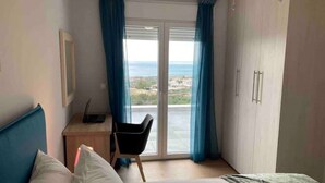 A bedroom with a bed, a desk, and a chair. There is a view of the outdoors through a window with curtains. - ZAX SEA VIEW 4 villa complex, Heated pool and 8 bedrooms (ierapetra)