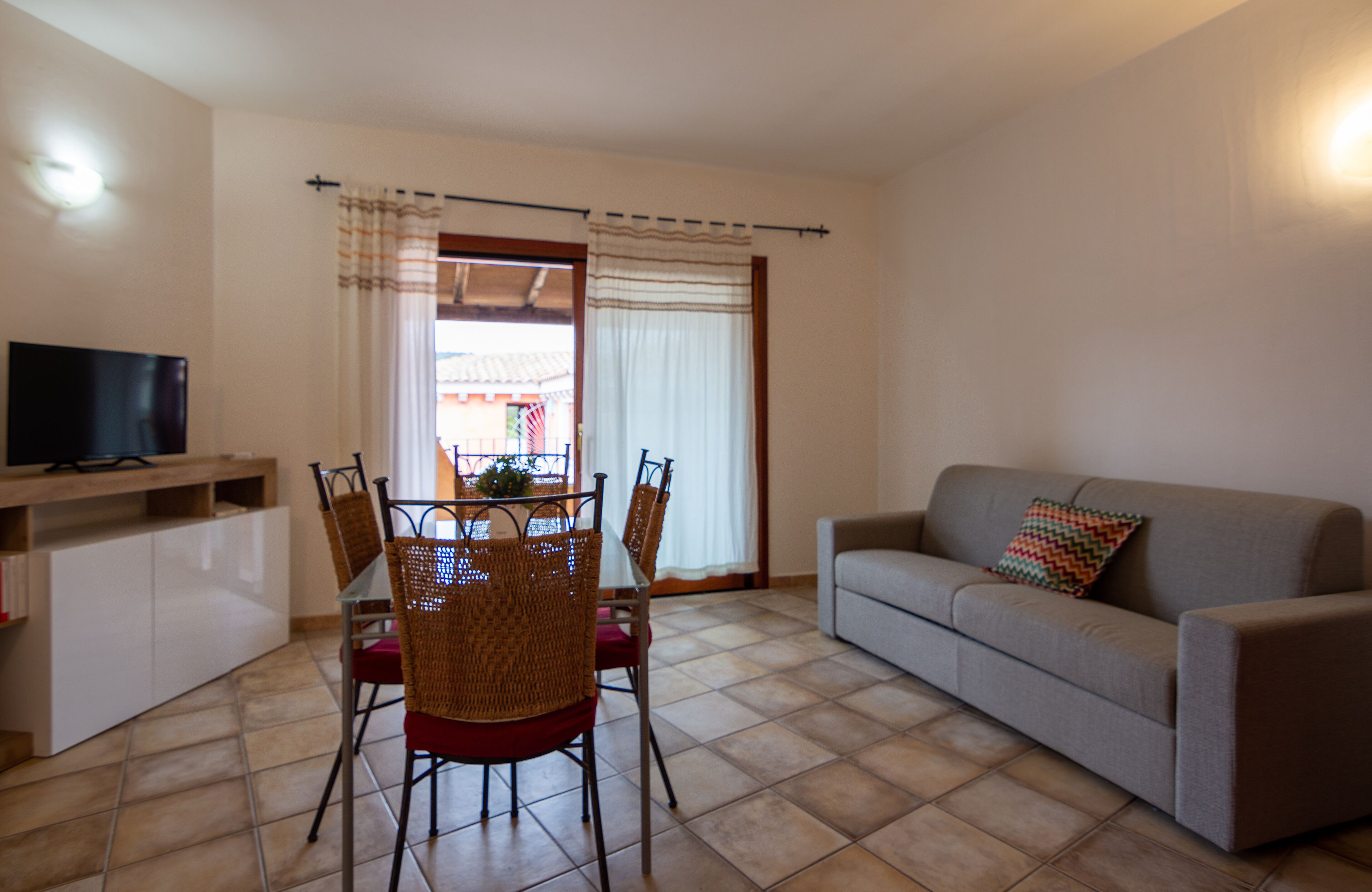 Una sala de estar con un sofá, un televisor, una mesa de comedor con sillas y una ventana con cortinas.