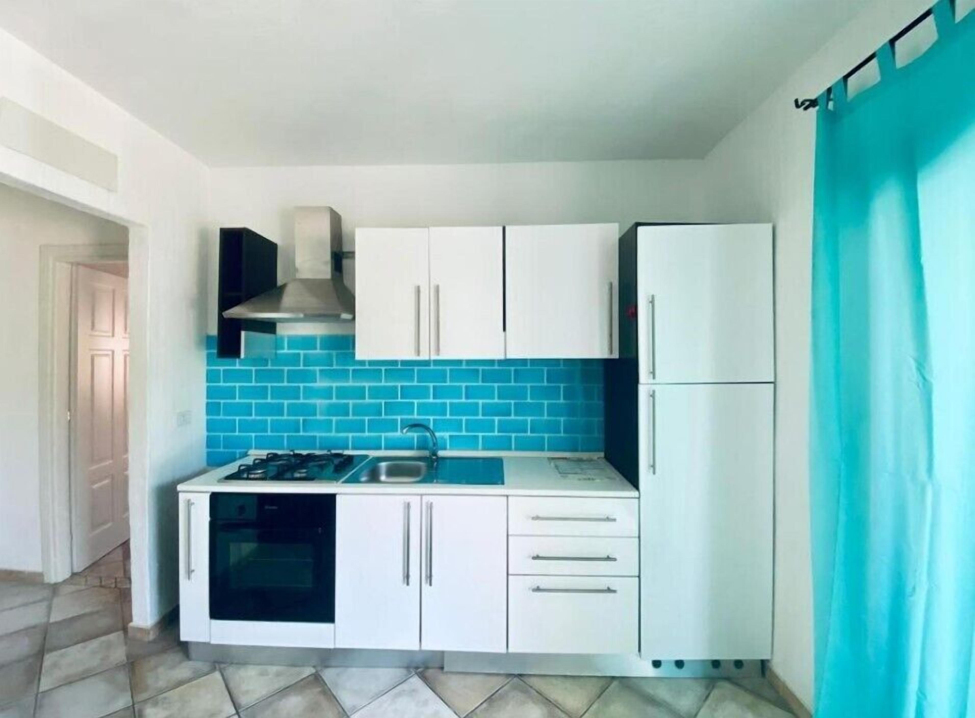 Une cuisine de taille réduite avec des meubles blancs, une cuisinière à gaz et un crédence recouverte de carreaux bleus.