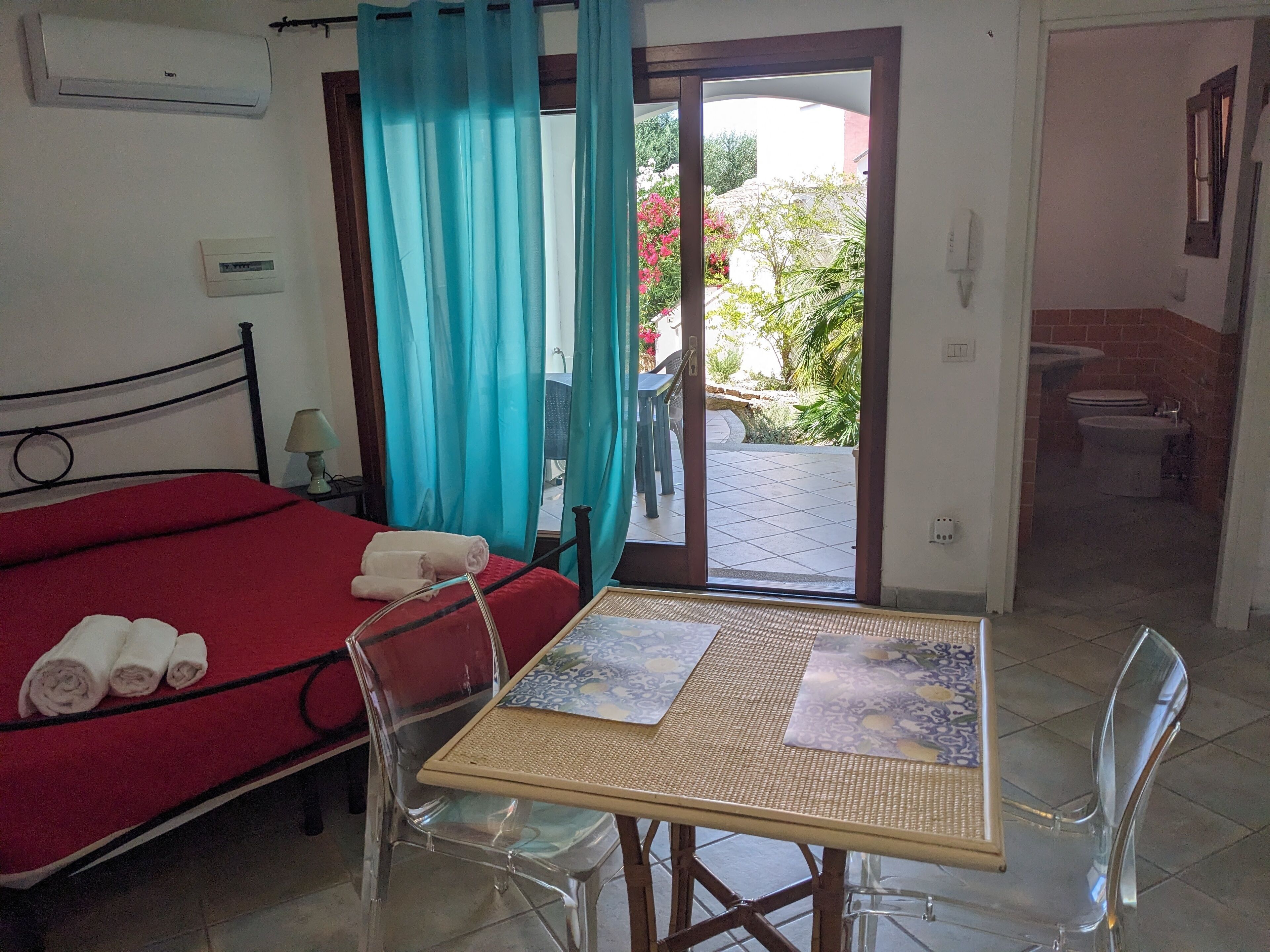 A room with a bed, a table, and a view of the outside.