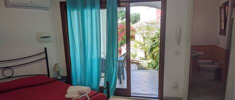 A room with a bed, a table, and a view of the outside.