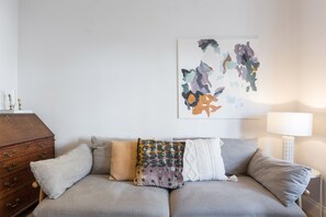 A neutral-toned living room with a grey sofa, a wooden chest of drawers, and a white lamp. - Newly renovated large 4/5 bedroom house with garden. (London)