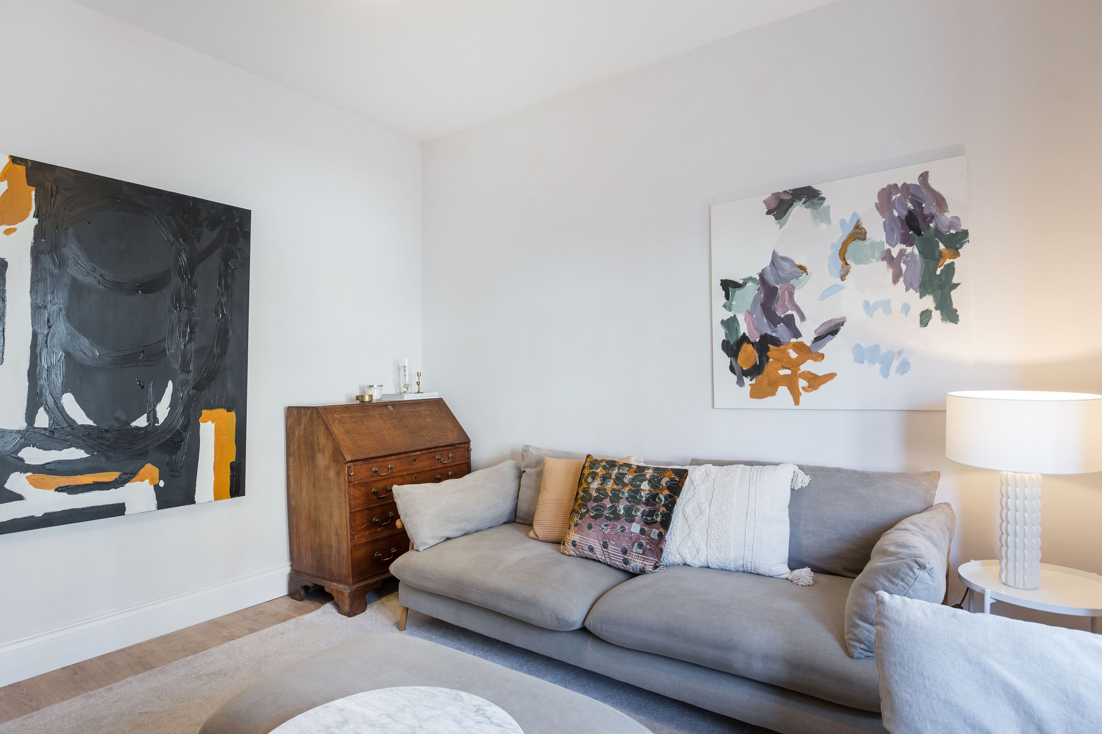 A living room with a grey sofa, a wooden cabinet, and abstract paintings on the walls.