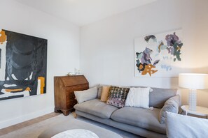 A living room with a grey sofa, a wooden cabinet, and abstract paintings on the walls.