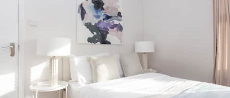 Un dormitorio moderno con una cama, dos mesitas de noche y un cuadro abstracto colgado en la pared.