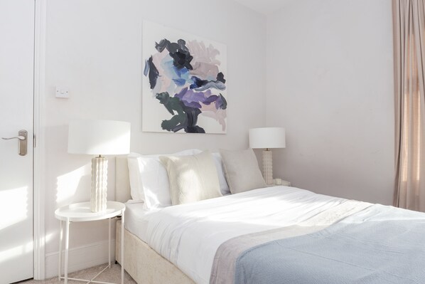 A modern bedroom with a bed, two bedside tables, and a wall-mounted abstract painting.