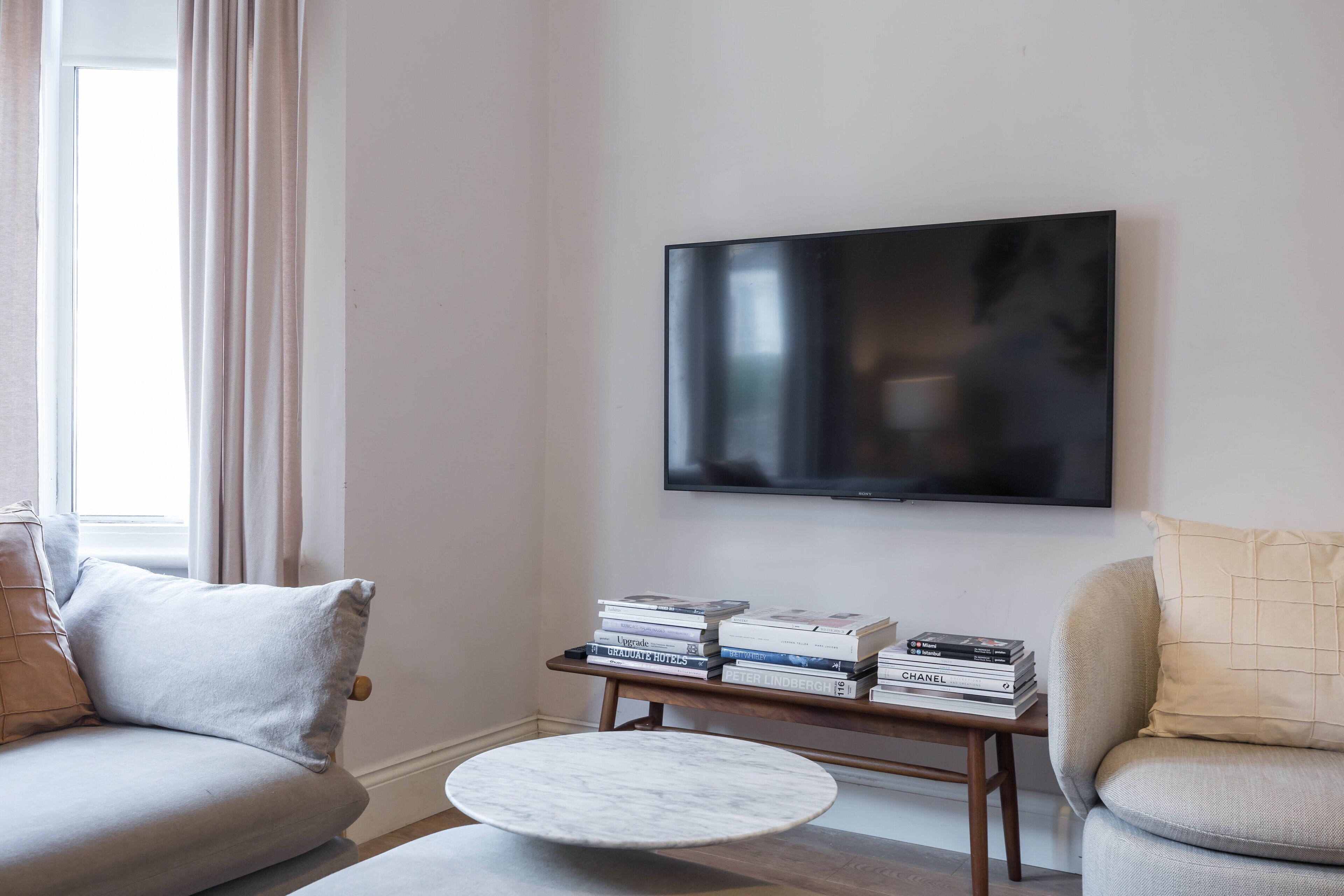 En stue med et fladskærms TV, et sofabord og en stabel bøger på et træ sidebord.