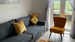 Una sala de estar con un sofá gris, dos cojines amarillos, un sillón color mostaza y una lámpara.