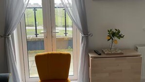 Una habitación con una silla amarilla, una mesita con un jarrón de flores y un televisor Samsung montado en la pared.