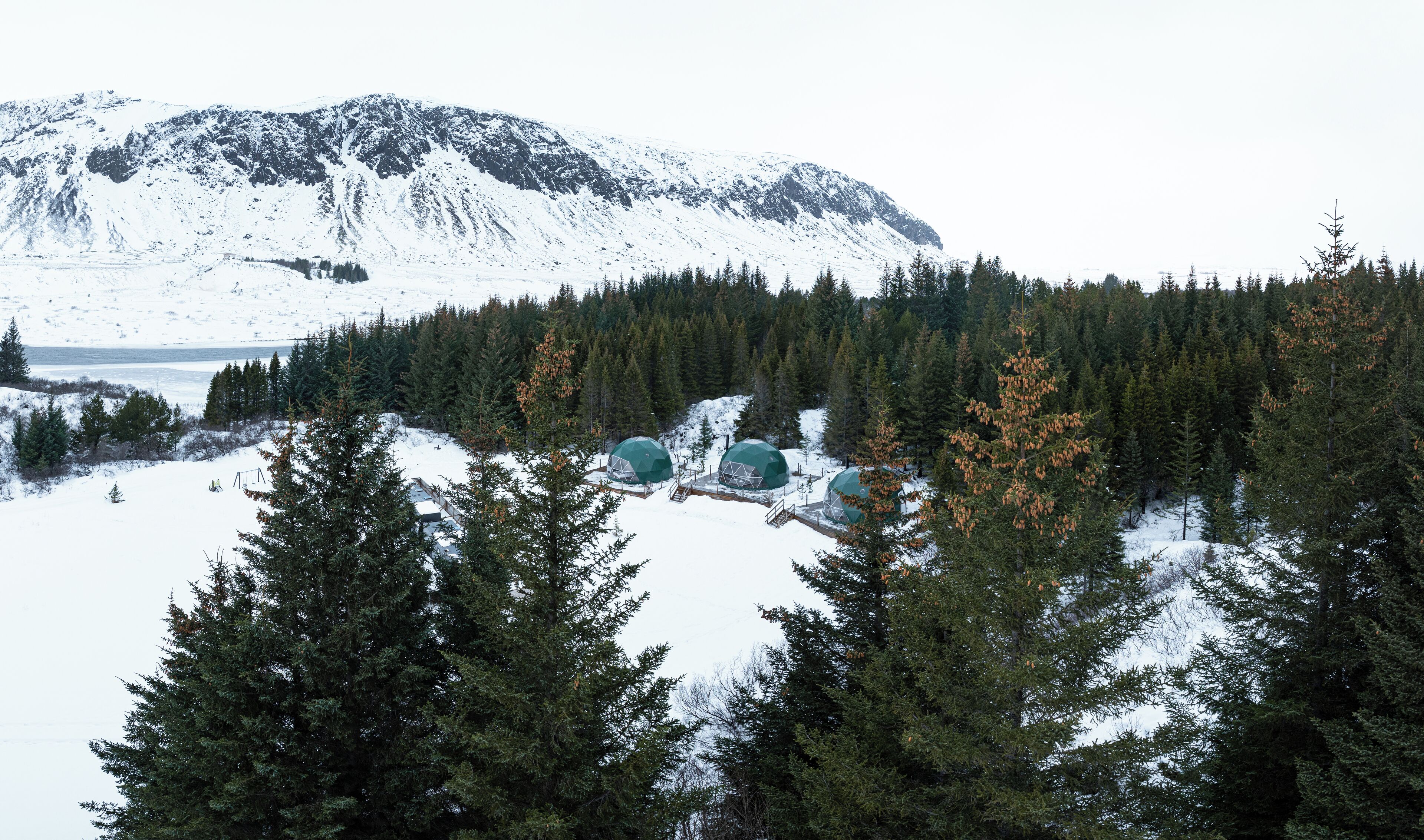 A snow-covered landscape with a mountain in the background and a forested area with dome-shaped structures.