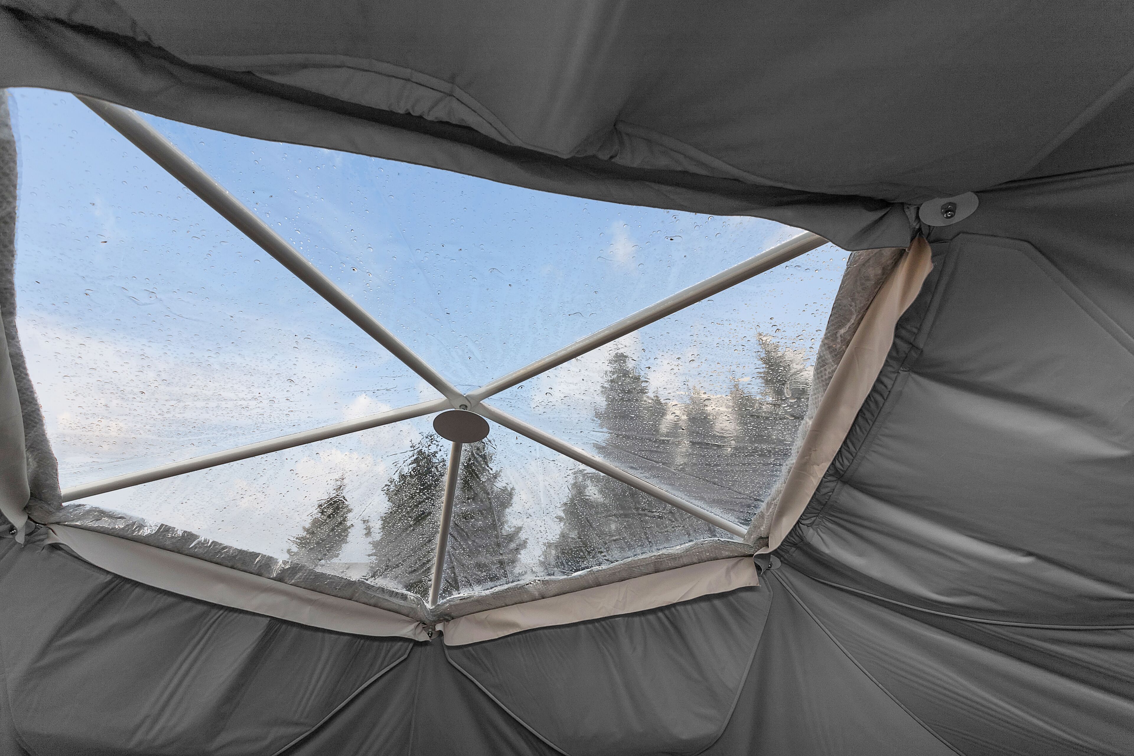 Une tente dotée d’une fenêtre transparente, offrant une vue sur les arbres et un ciel nuageux.