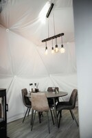 Una habitación tipo tienda de campaña con una mesa redonda, cuatro sillas y una lámpara colgante.