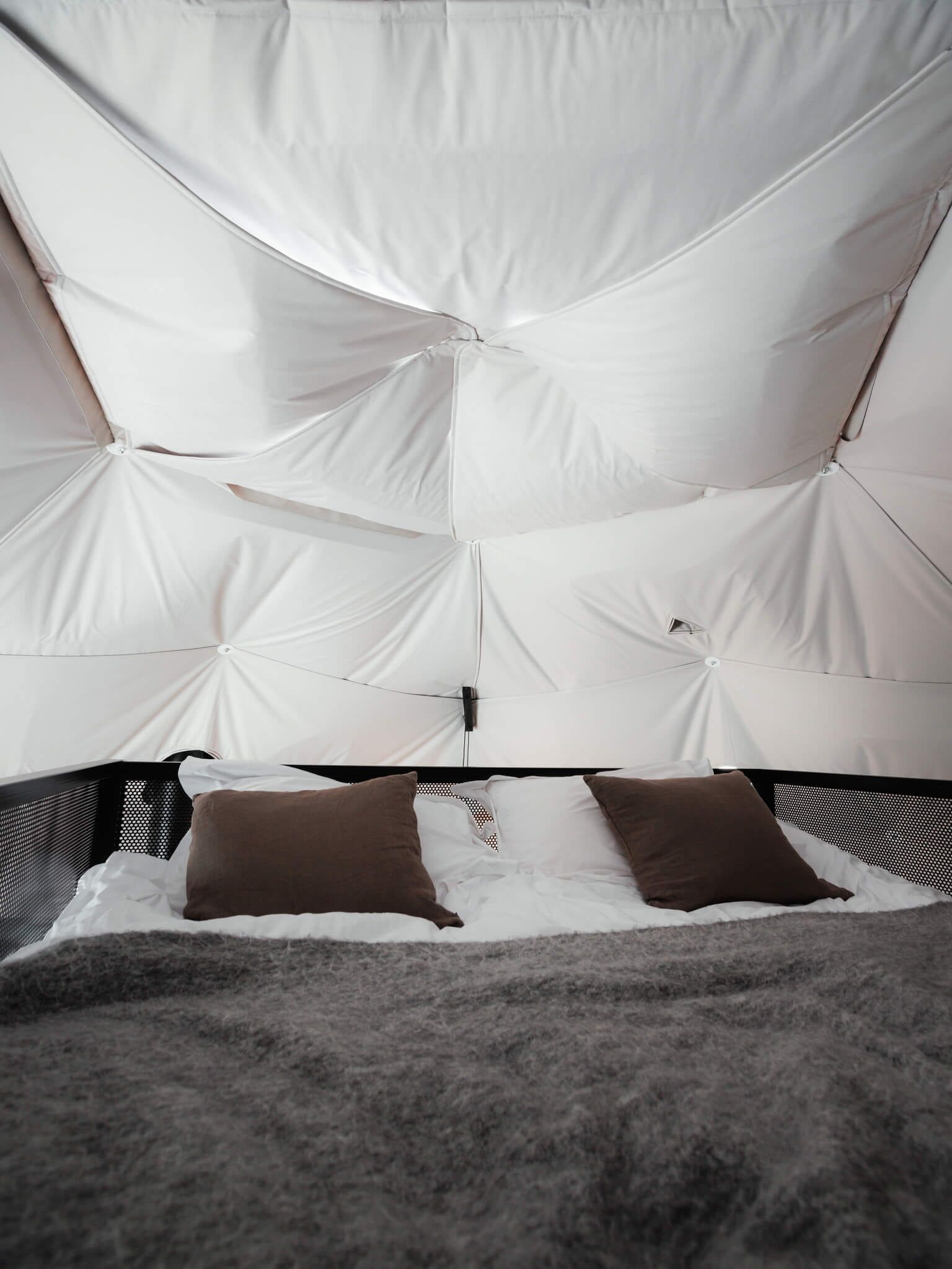 A bed with a tufted headboard, two brown pillows, and a grey blanket.
